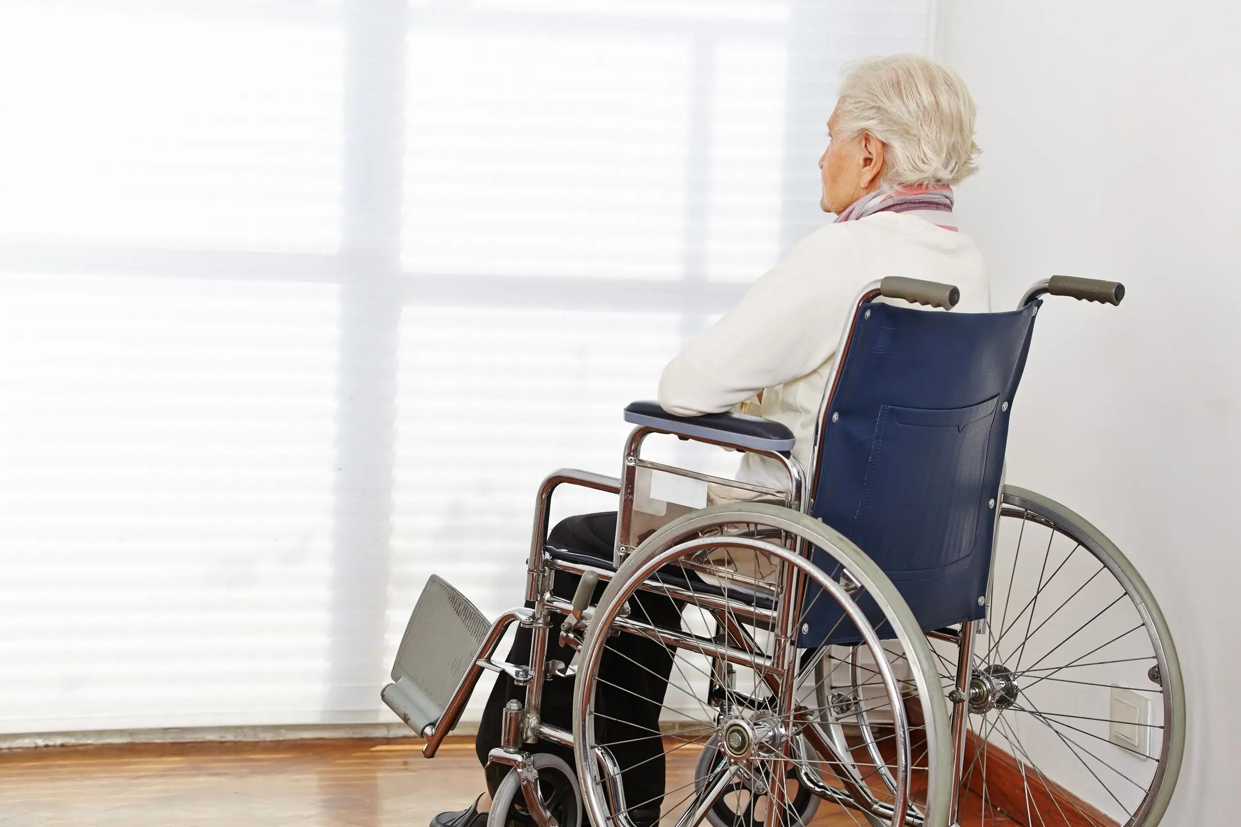 An elderly woman in a wheelchair looking out a window